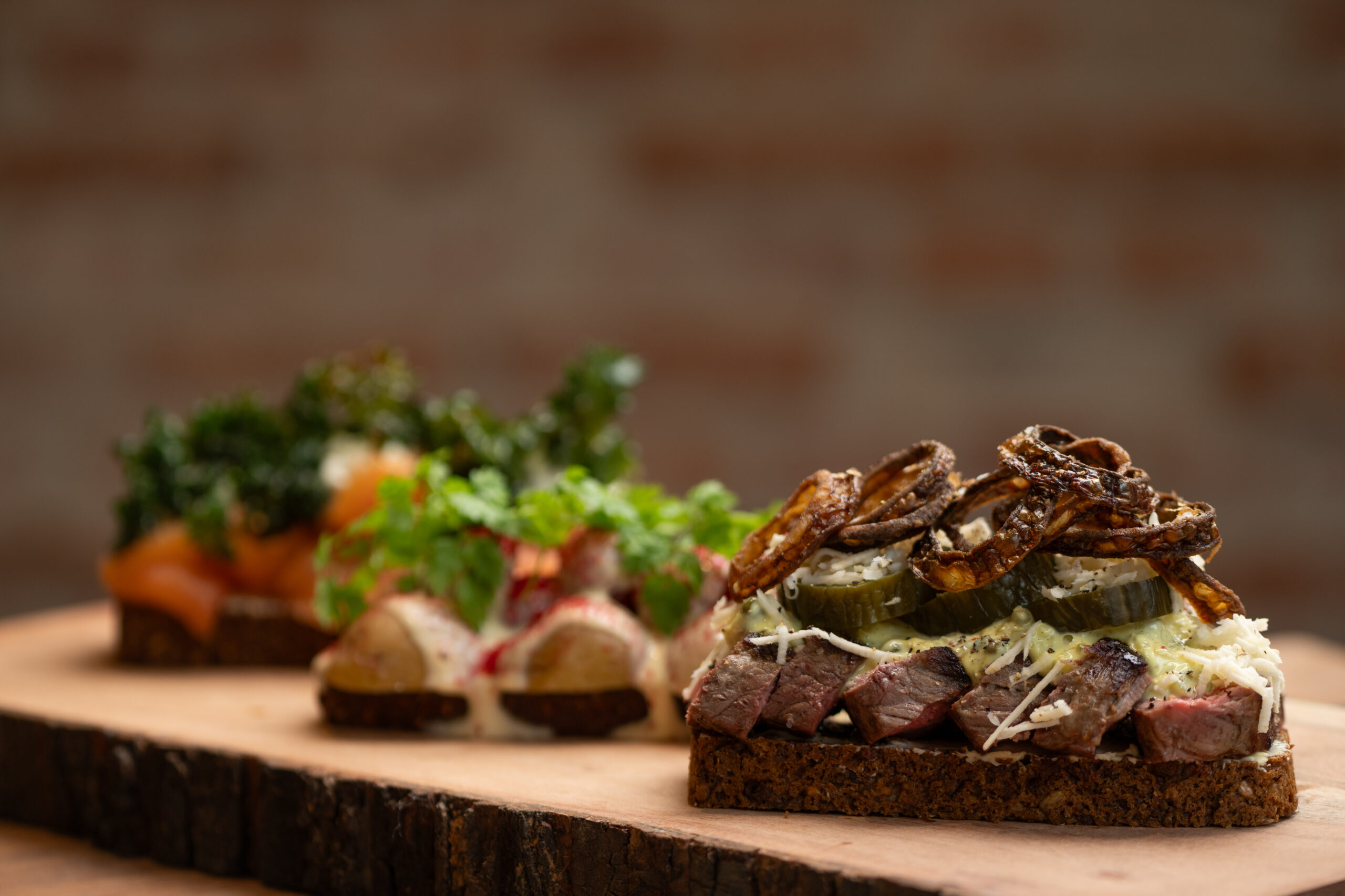 Tre smørrebrød med forskelligt fyld på træplade.