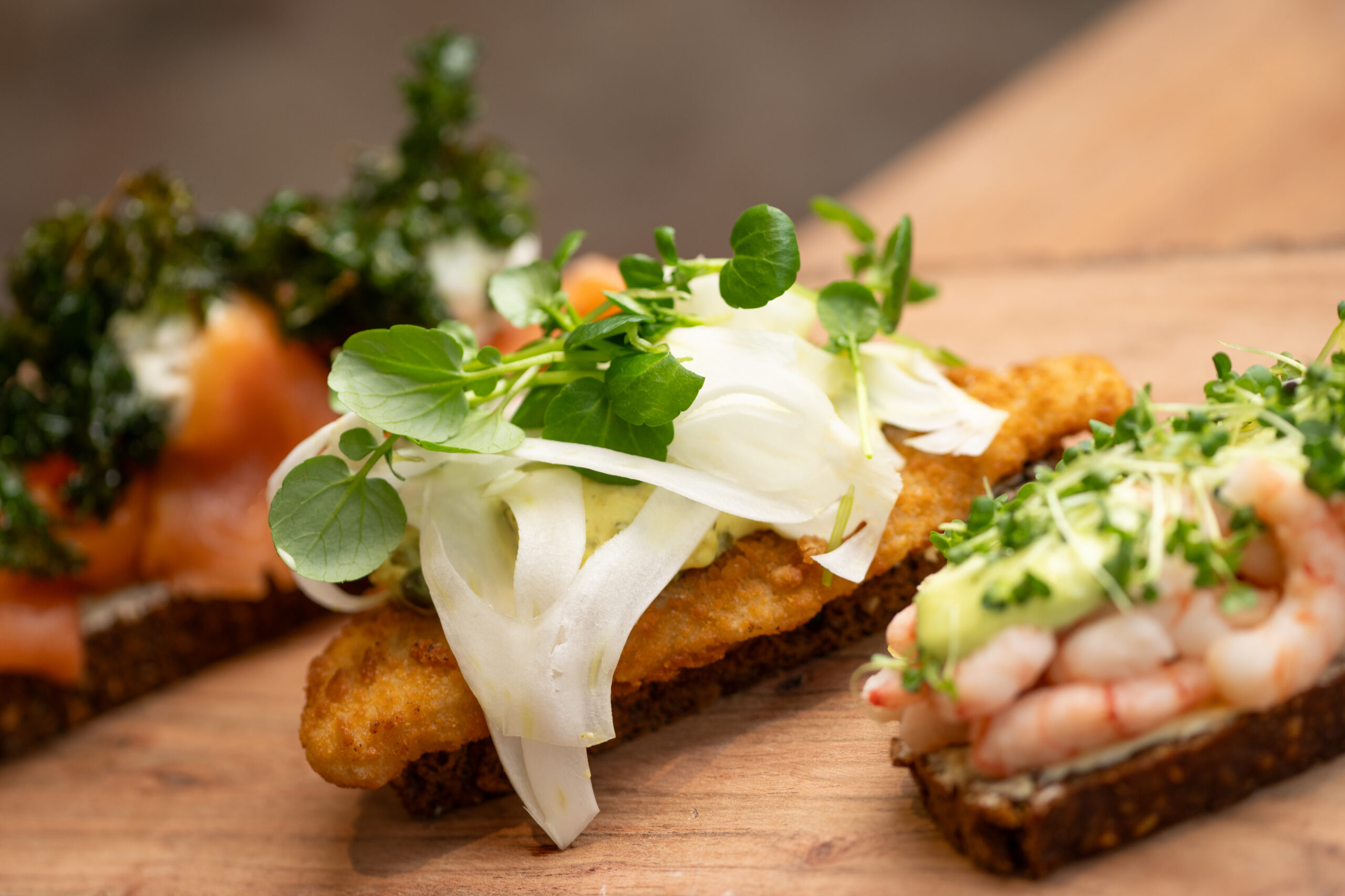 Lækkert smørrebrød med fisk og rejer på træplade.